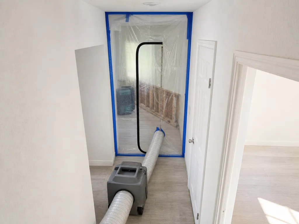 A hallway sealed off with plastic sheeting and a zipper door, an air scrubber ducted into the work area during mold remediation