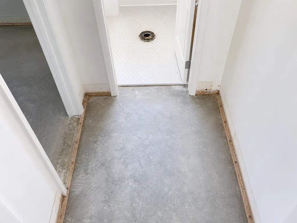 A hallway with carpet and pad removed to bare concrete outside a bathroom whose toilet has been pulled after a sewage backup